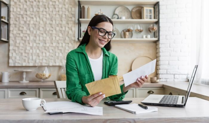A young beautiful student girl in glasses and a green shirt received a letter of invitation to the university. received notification of admission. He sits at home, opens the envelope, is happy.